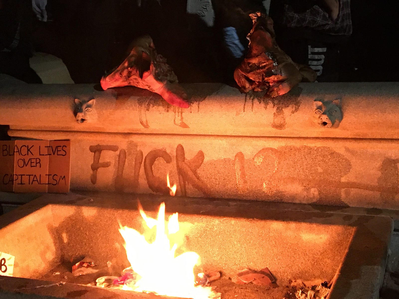 pigs heads being roasted on elk statue base with “fuck 12” graffiti and “black lives over capitalism” sign