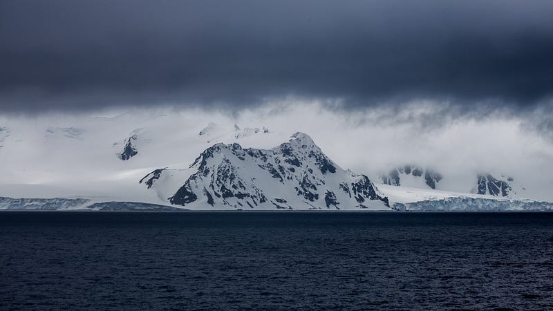 mountain towering over ocean, cloudy grey sky