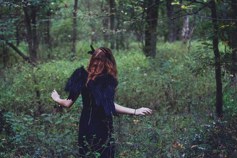 a woman wearing black angel wings wandering through the forest
